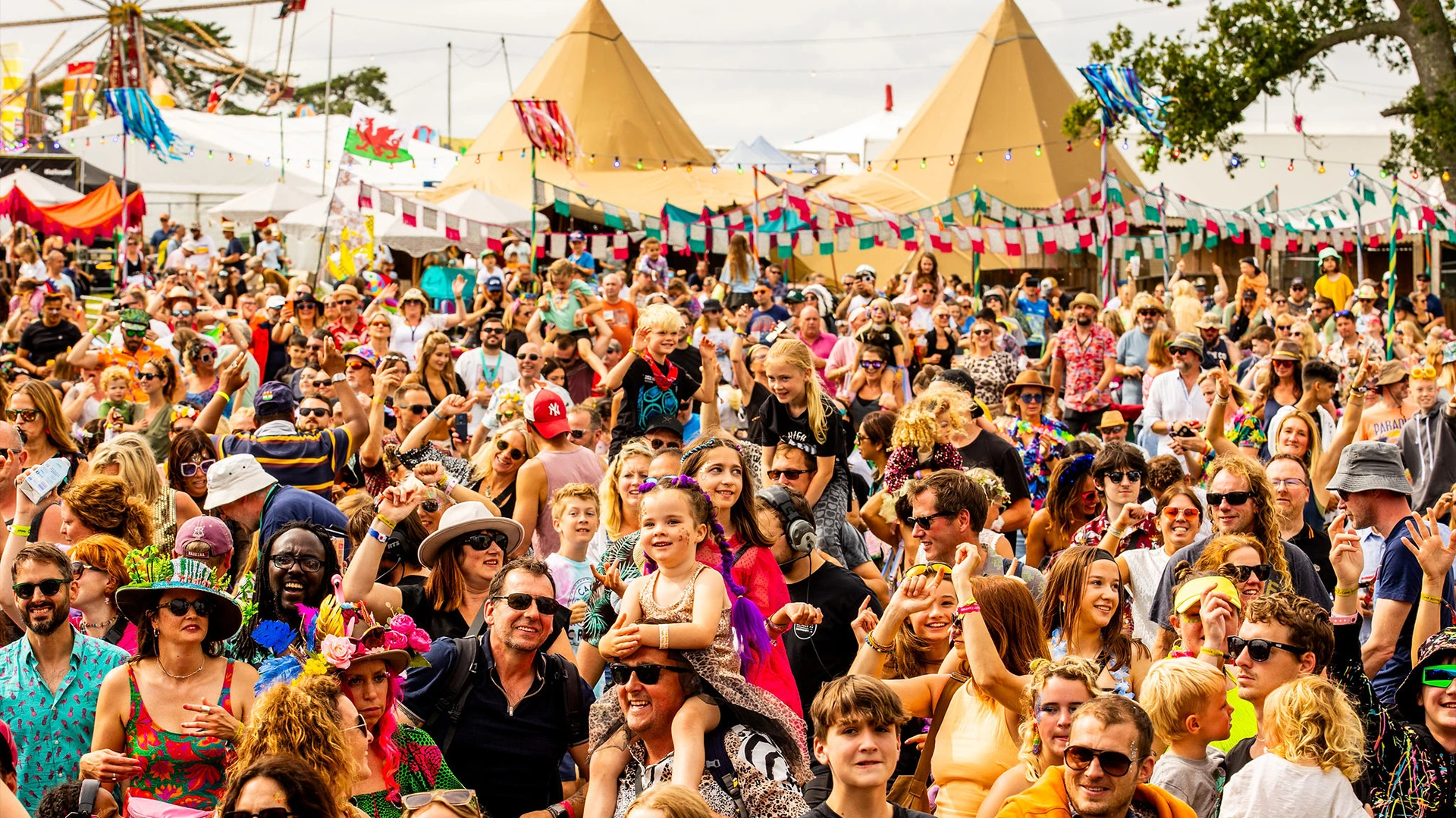 Large festival crowd gathered beneath tipis and colourful bunting