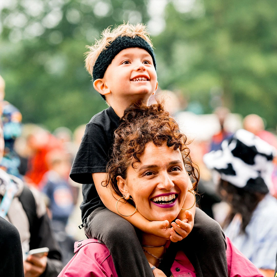 Smiling woman carrying a child on her shoulders at a festival