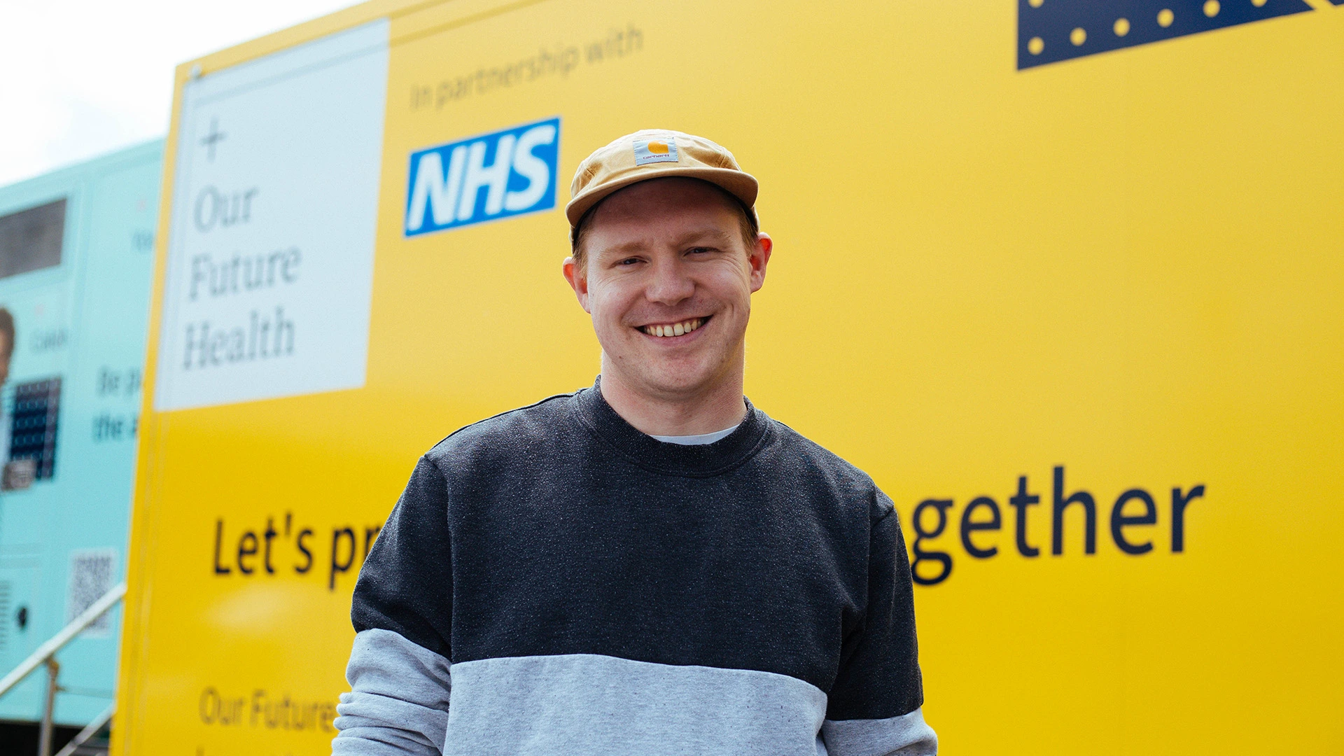 Smiling man in a cap in front of the Our Future Health van