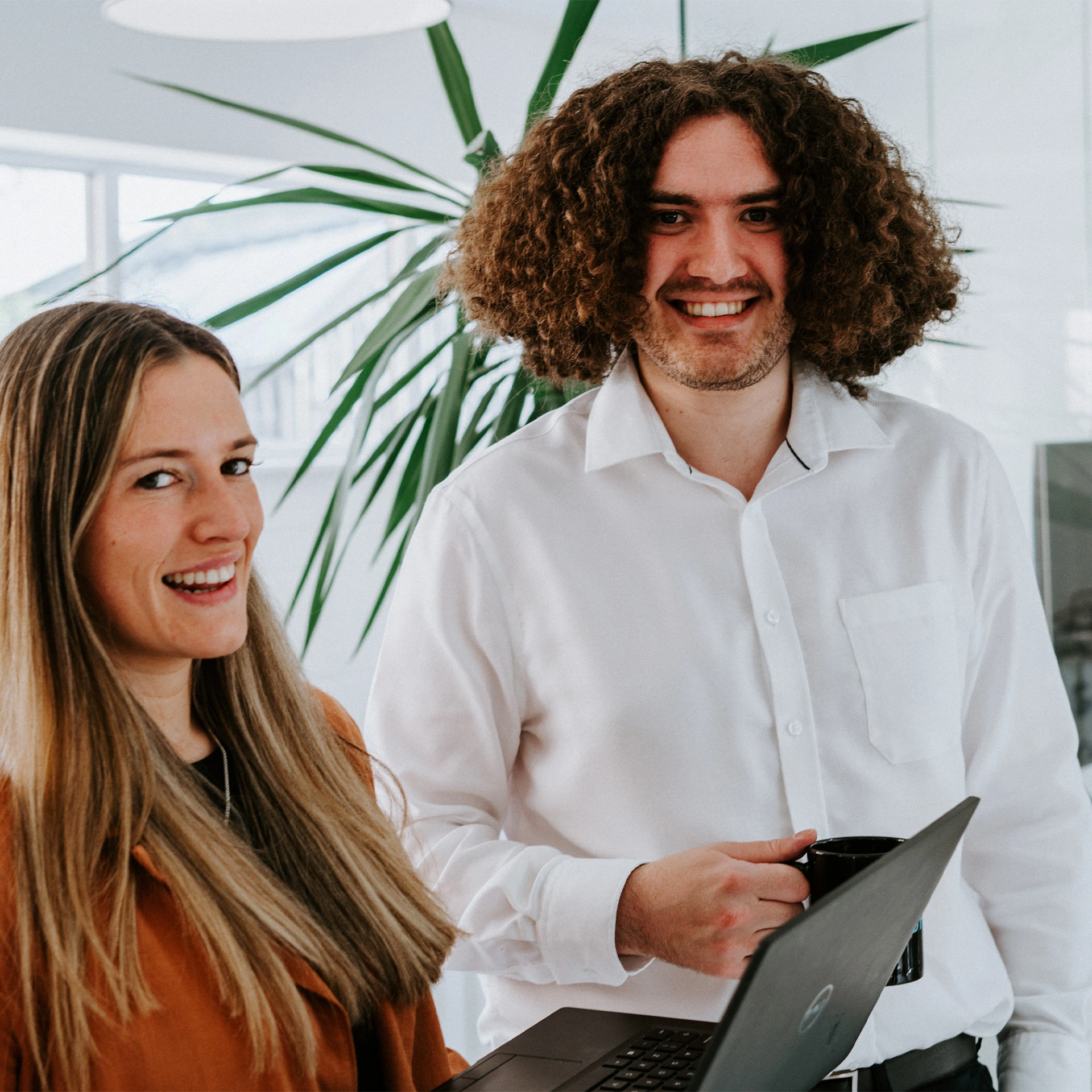 Two smiling colleagues with a laptop in a bright office
