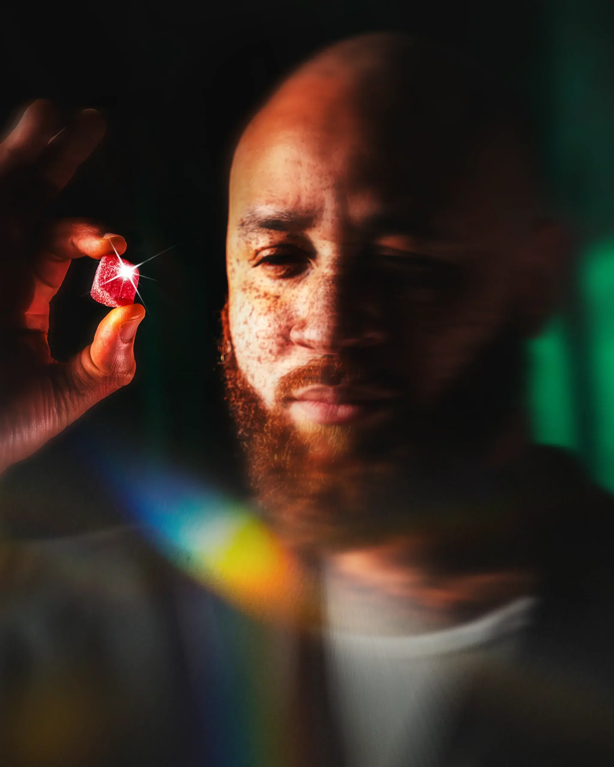 Man holding a crystal that casts rainbow light across his face