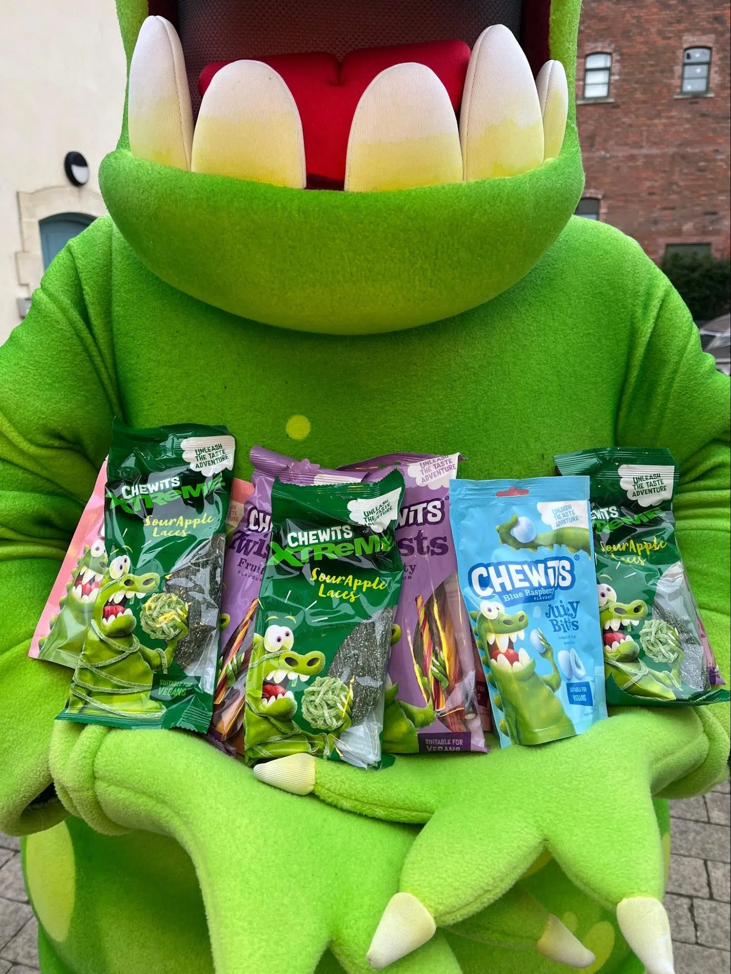 Green crocodile mascot holding packets of Chewits sweets