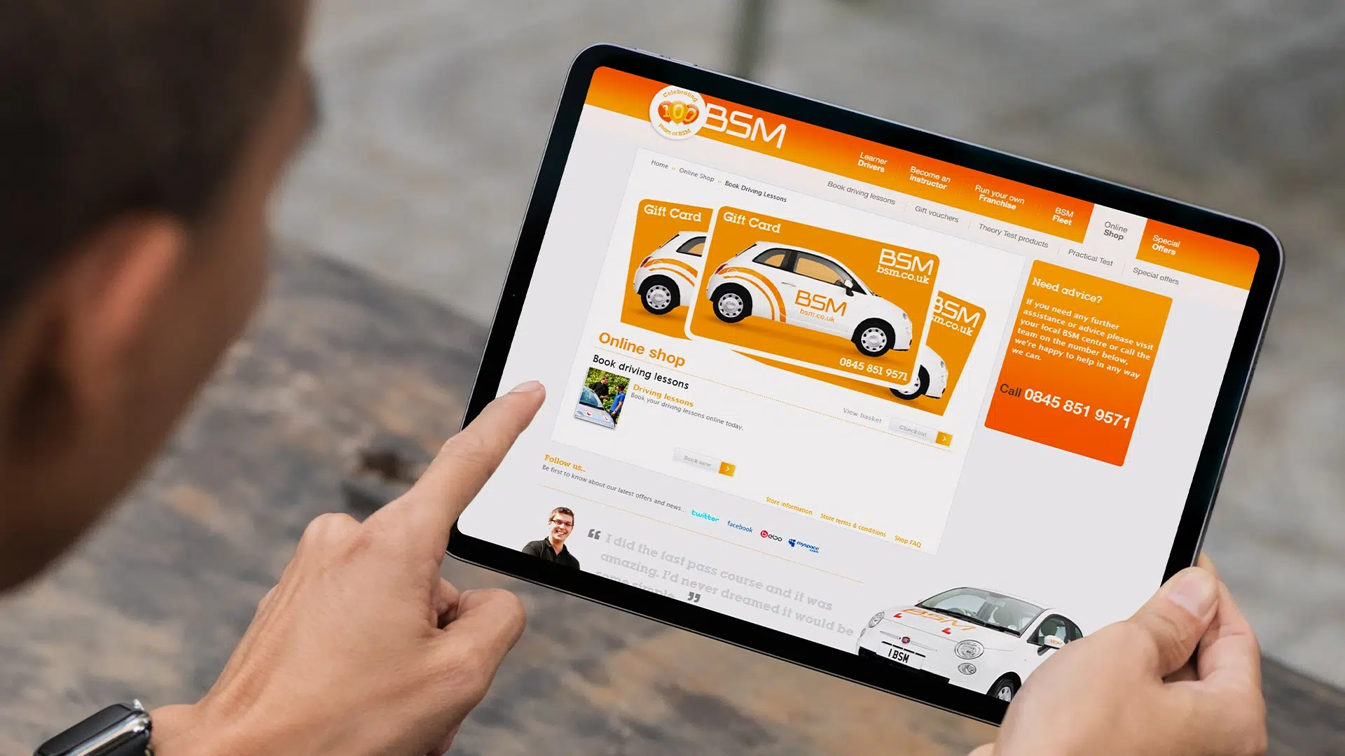 Hands holding a tablet showing the BSM driving school website