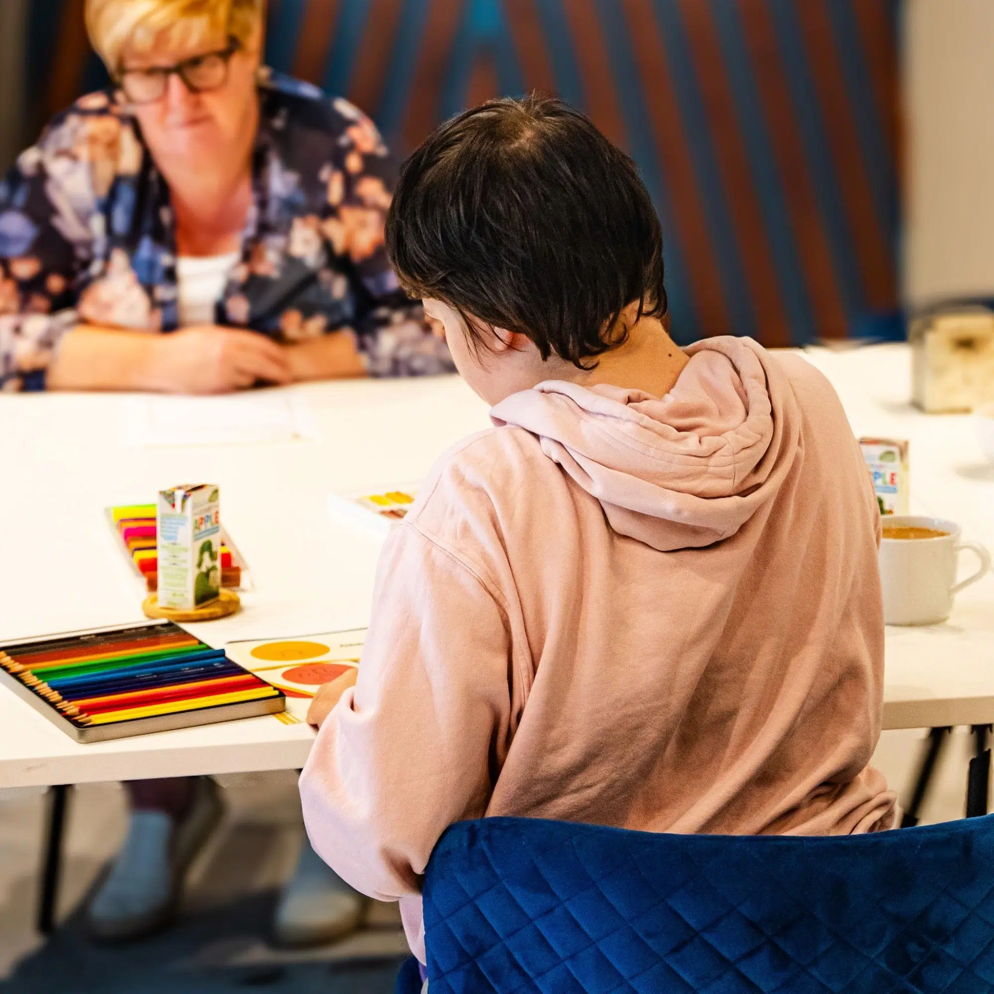 Two people at a workshop table with coloured pencils