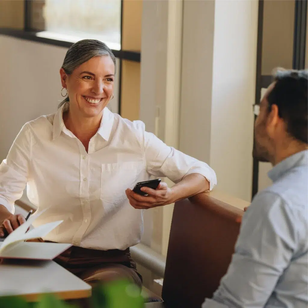 Smiling woman holding a phone during a meeting with a colleague