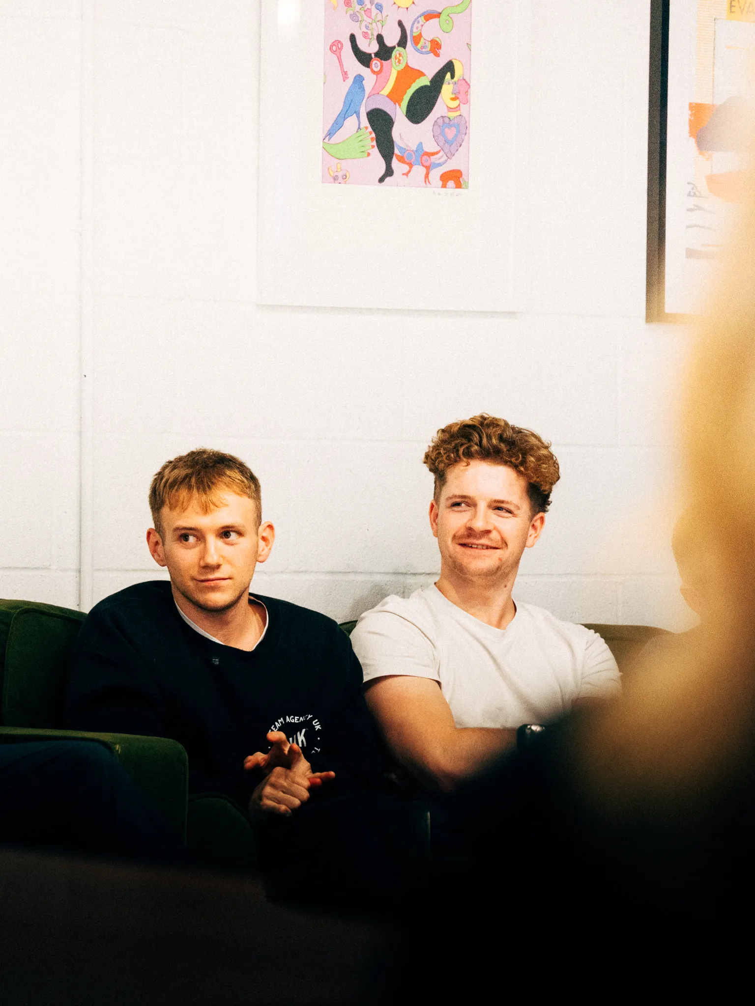 Two AgencyUK team members smiling on a sofa in the studio